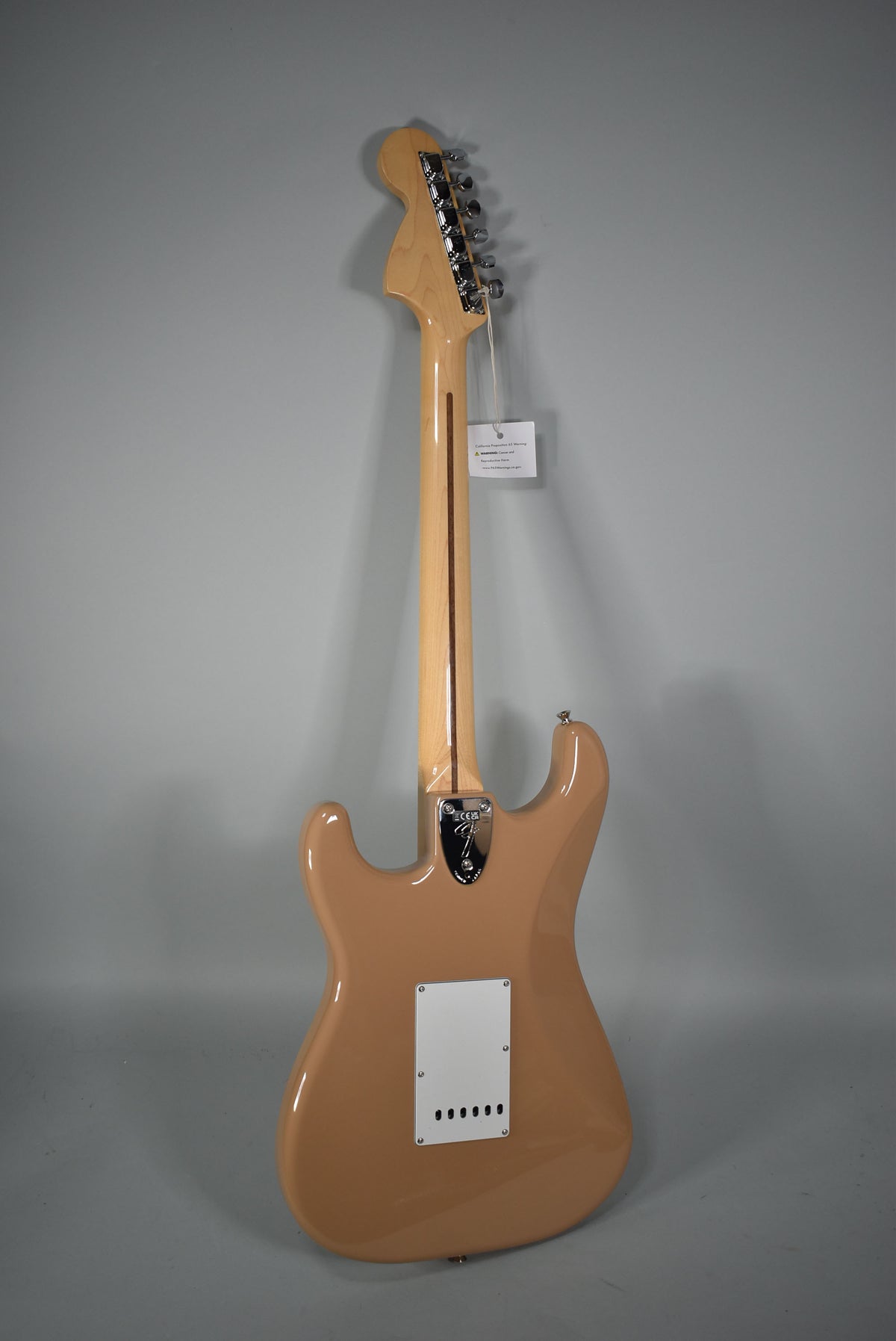 The full back of a Sahara Taupe Stratocaster is shown, with a light maple neck, chrome tuners, and a white tremolo cover.