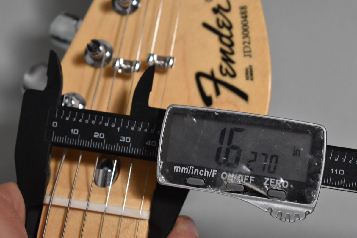 A digital caliper measures the guitar's nut width at 1.627 inches, with the headstock and tuning pegs visible.