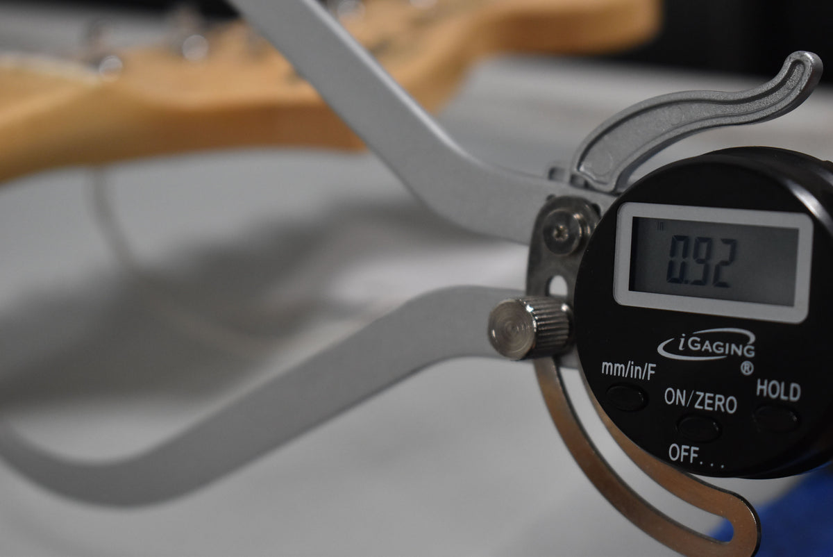 A close-up of a digital caliper measuring the guitar's neck, displaying "0.92" on its screen.