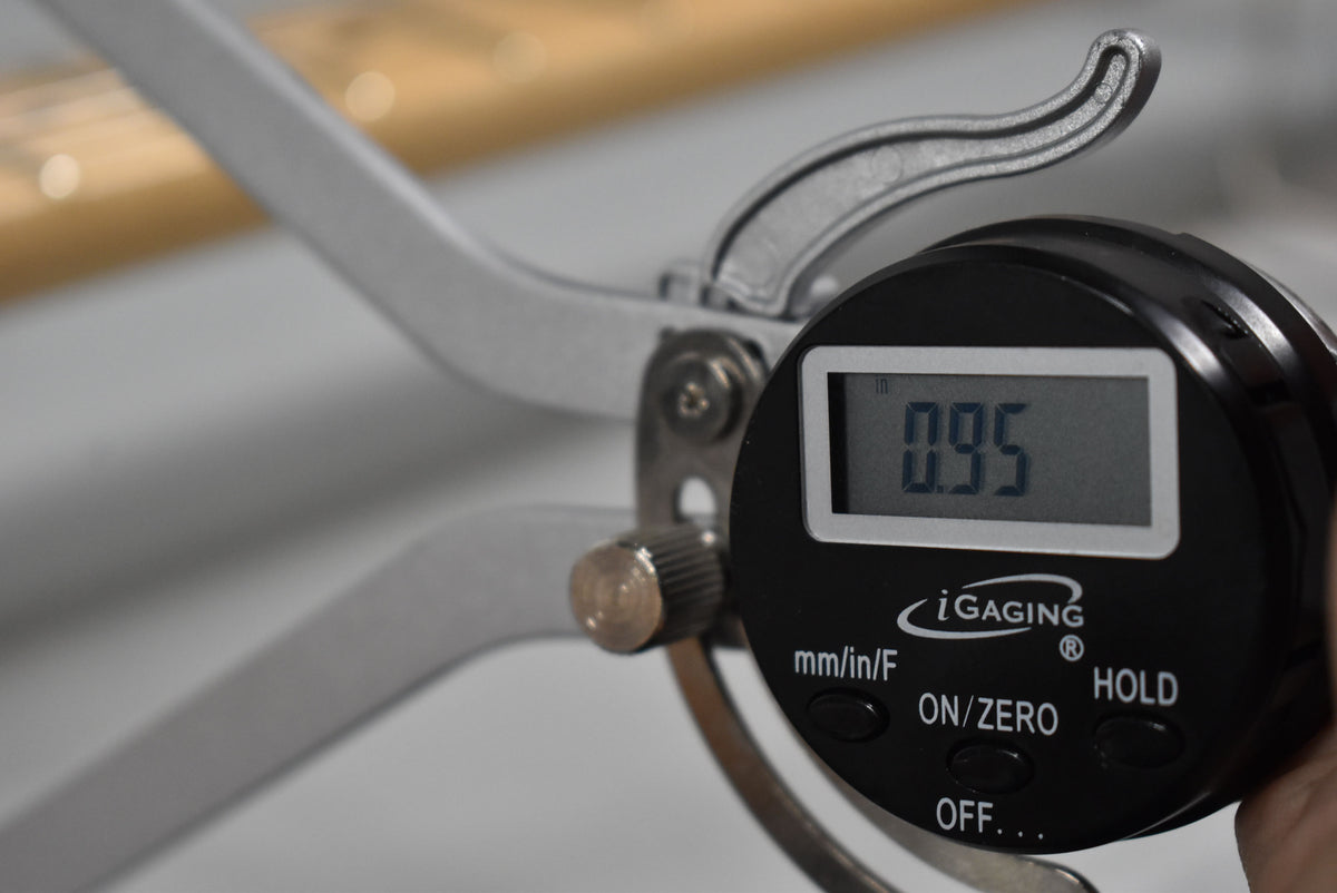 A close-up of a digital caliper measuring the guitar's neck, displaying "0.95 in" on its screen.