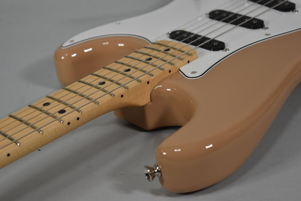 The Sahara Taupe Stratocaster's body and neck are shown from above, with a white pickguard and black single-coil pickups.