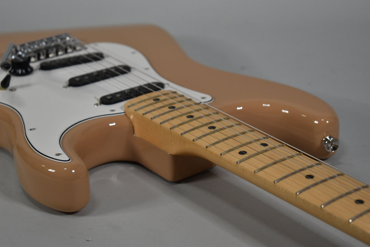 A Sahara Taupe Stratocaster, angled from the lower bout, showing its white pickguard, three black single-coil pickups, and maple fretboard.