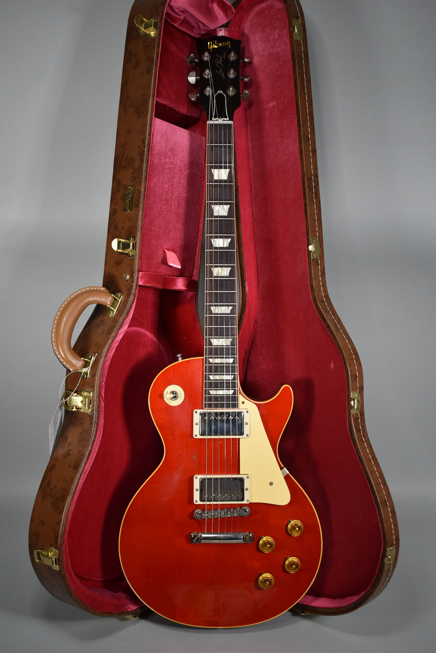 Full-length view of a cherry red electric guitar with cream binding, pickup rings, and pickguard, in a brown case with red lining.