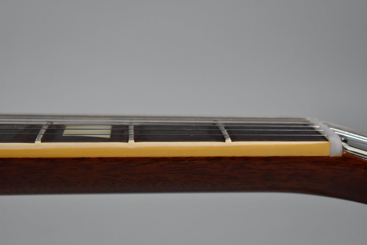 The guitar's dark brown neck and fretboard are seen from the side, with cream binding, trapezoid inlays, and a white nut.