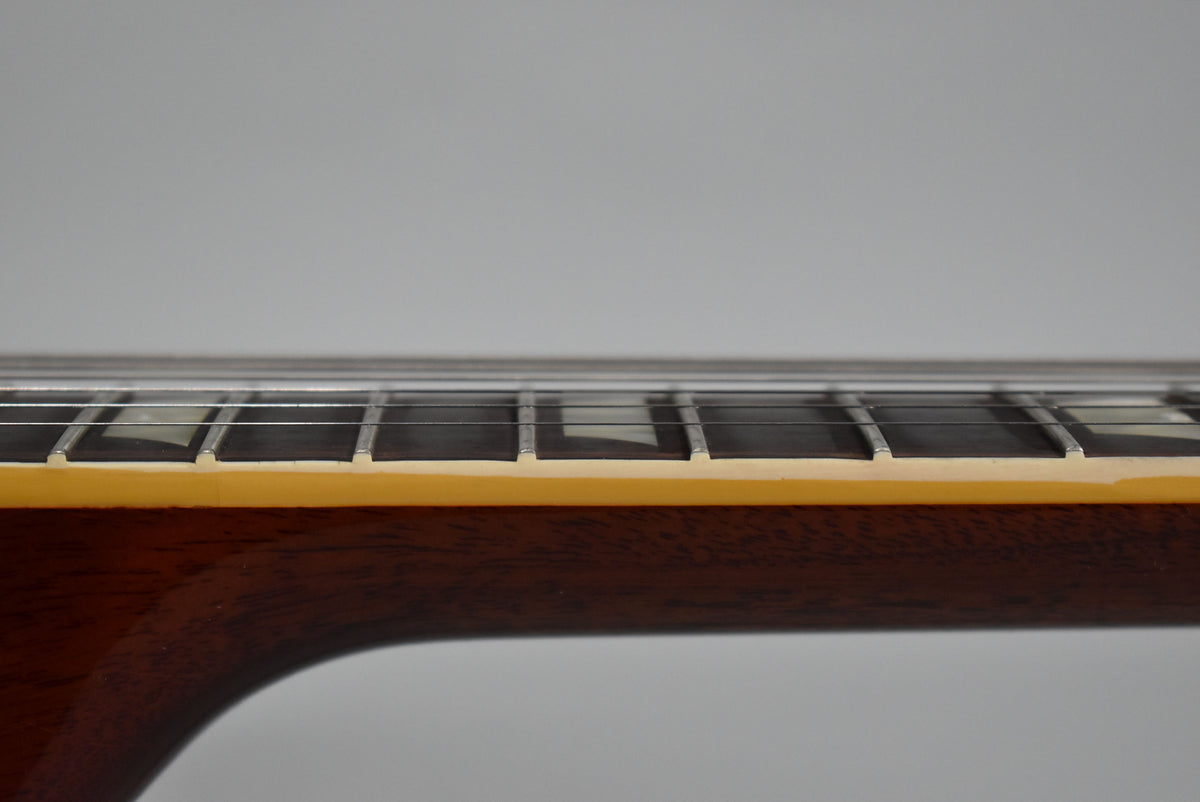 Close-up of the guitar's dark brown neck and fretboard, showing trapezoid inlays, frets, and strings from a side angle.