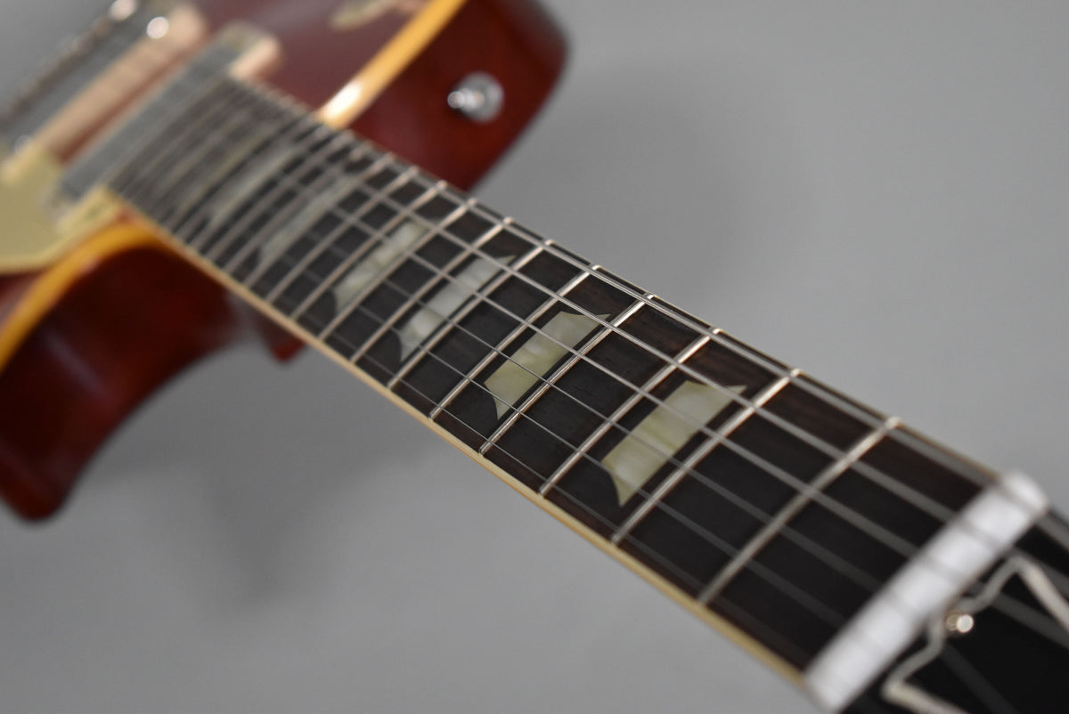 Close-up of the guitar's dark fretboard with trapezoid inlays, angled from the nut towards the cherry red body.