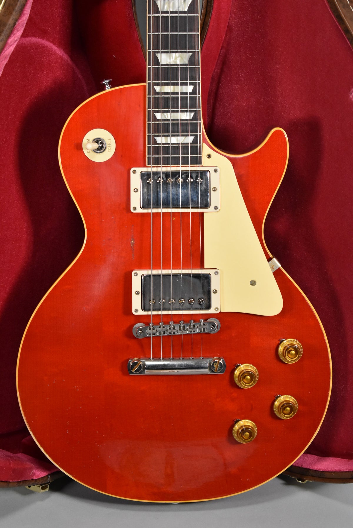 The cherry red Les Paul's body and neck are framed from the waist up, showing two humbuckers, a cream pickguard, and four gold knobs.