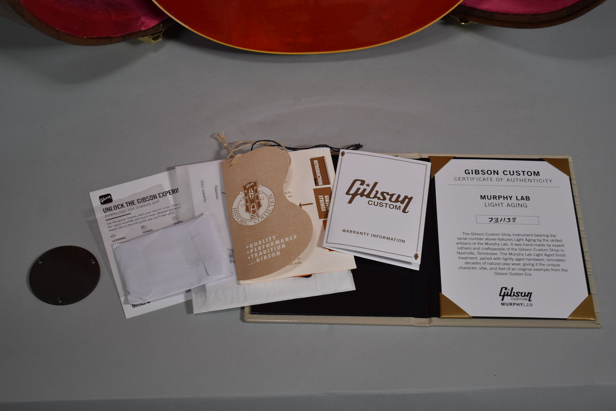 Overhead view of various white and tan paperwork, including a Gibson Custom certificate of authenticity, on a gray surface.