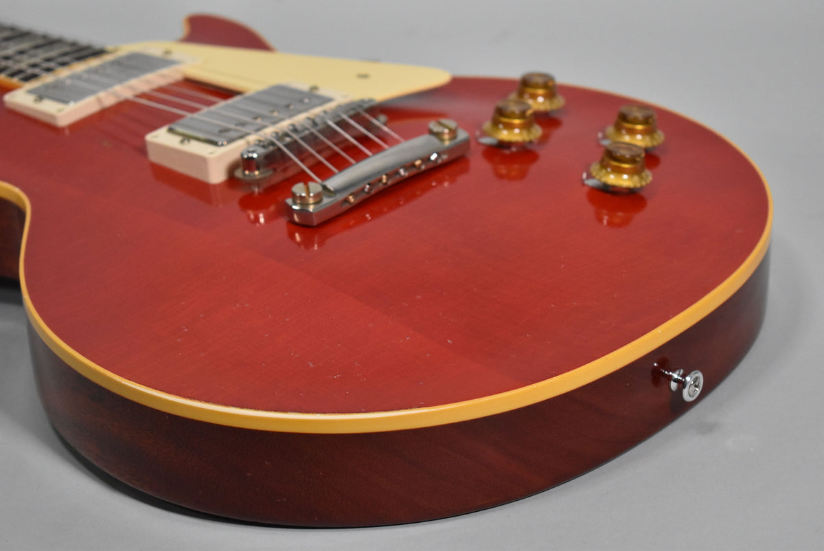 Close-up of the cherry red guitar body, showing the bridge, four amber control knobs, and cream binding with light relic wear.