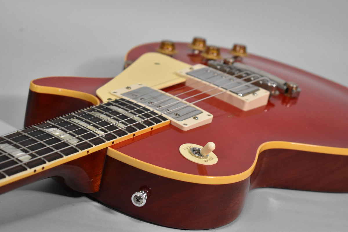 Close-up of a cherry red electric guitar, angled from the lower bout, showing the neck, pickups, and cream toggle switch.