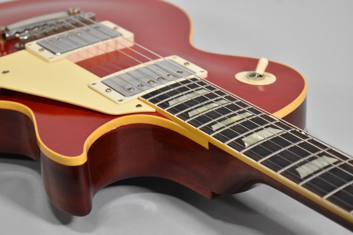 The cherry red Les Paul's body and neck are shown from the lower bout, revealing cream binding, pickguard, and pickup rings.