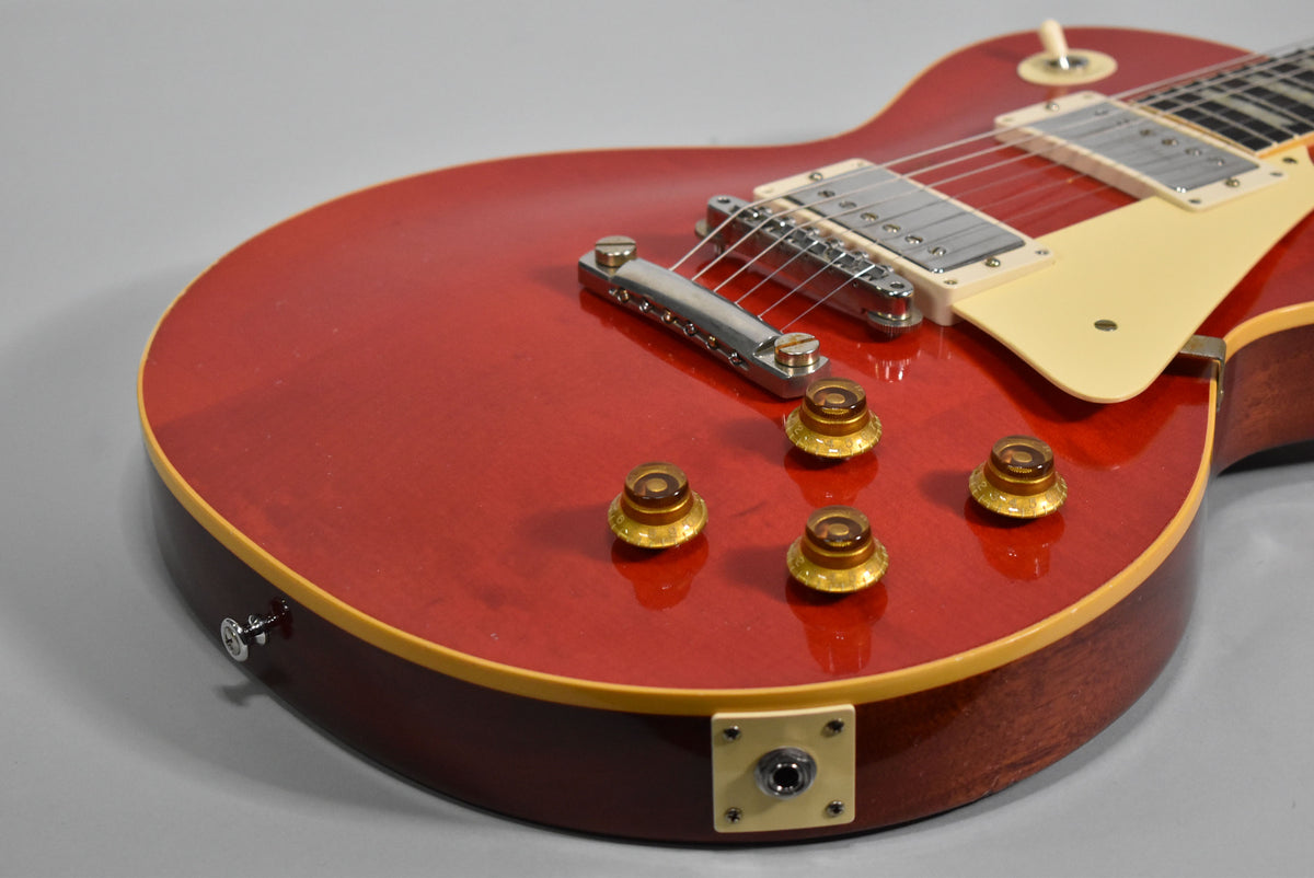 The upper body of a cherry red guitar, showing the bridge, four amber control knobs, cream pickguard, and output jack.