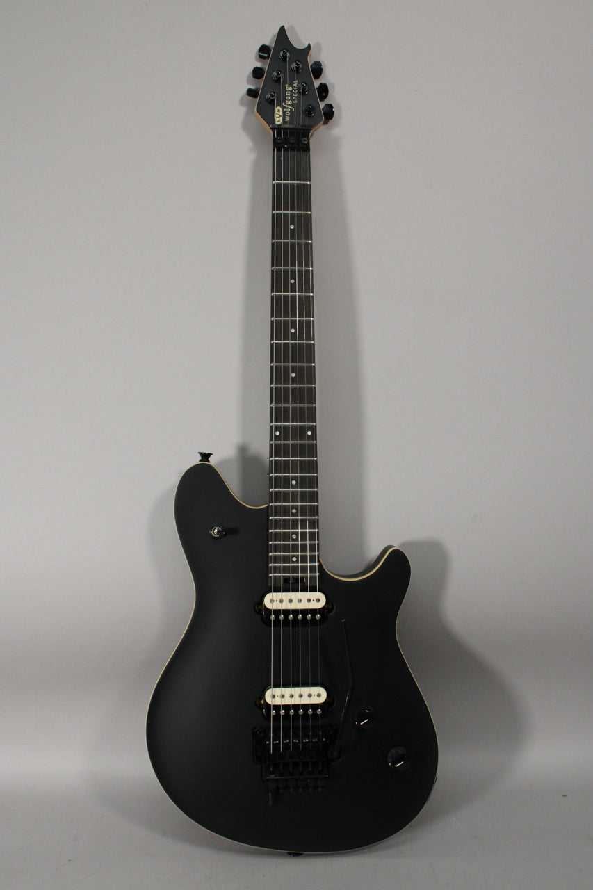 Full-length view of a matte black electric guitar with cream binding, black hardware, and two cream-colored humbucker pickups.