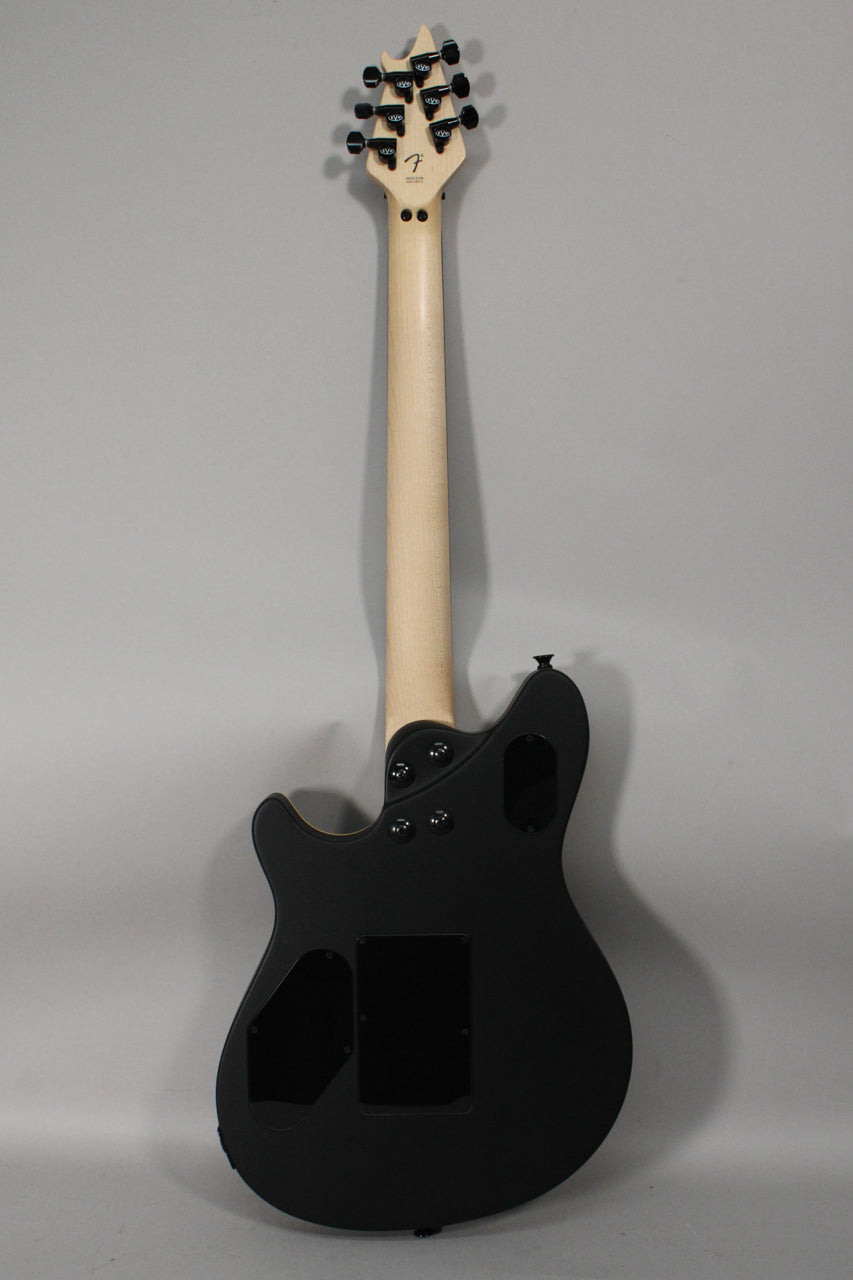 The back of a matte black electric guitar with a light maple neck, black tuners, and three control cavity covers.