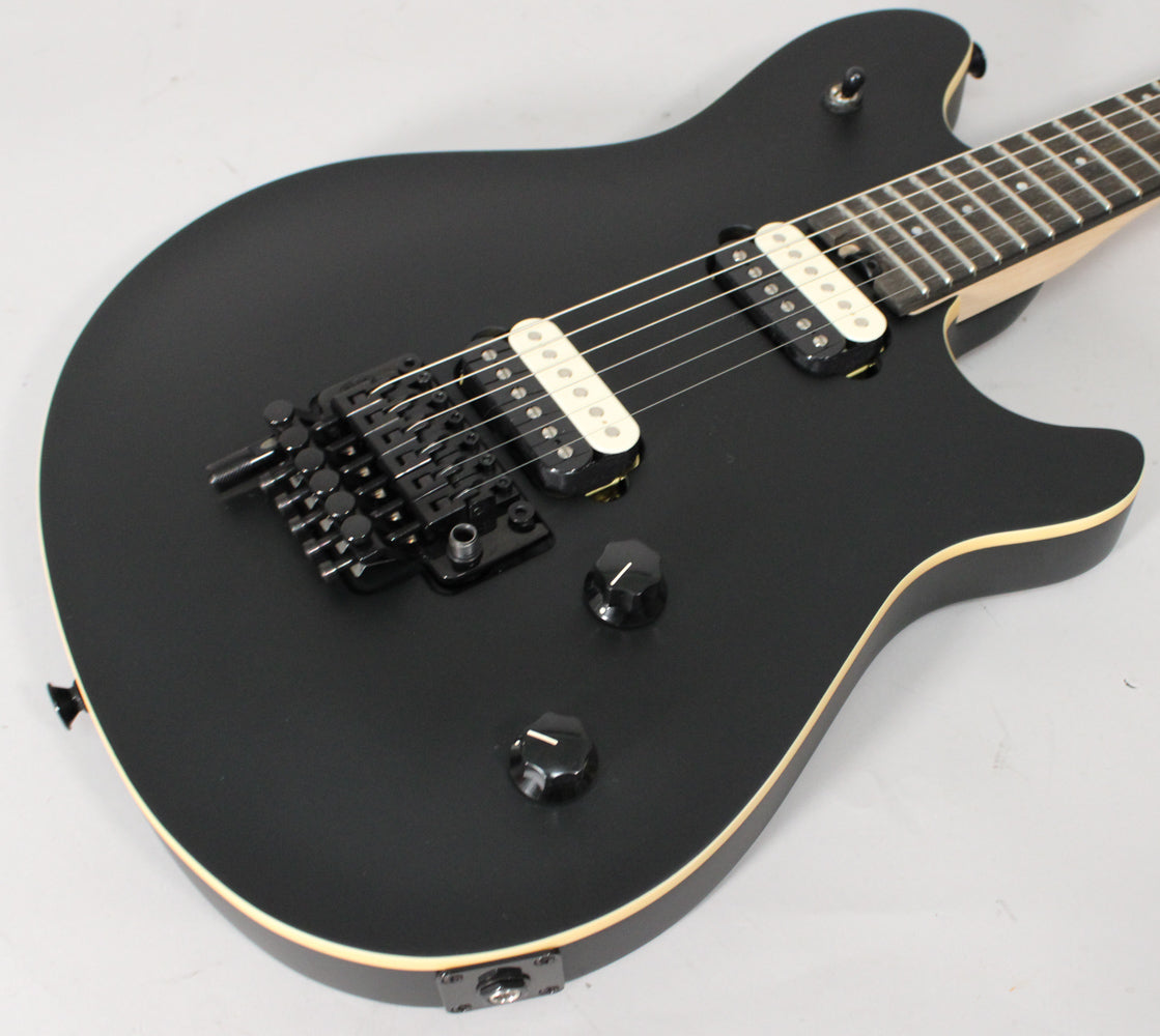 Matte black electric guitar, angled from above, showing the body, bridge, two cream humbuckers, and two black control knobs.