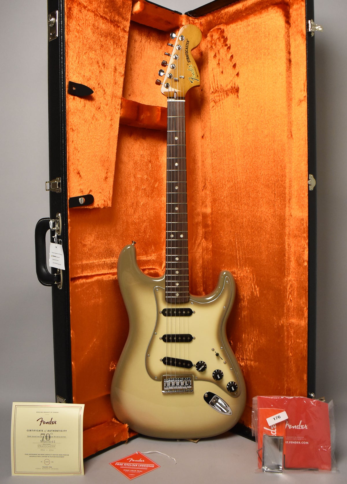 A full-length Antigua Stratocaster with a dark brown fretboard and black pickups rests in an open black case with orange plush lining.