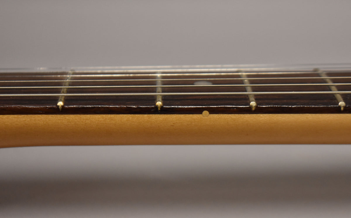 Close-up of the guitar's neck and dark fretboard, showing five frets, strings, and a single light-colored side dot marker.