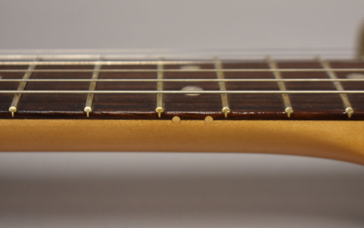 Close-up of the dark rosewood fretboard and light maple neck, showing the first few frets and side dots.