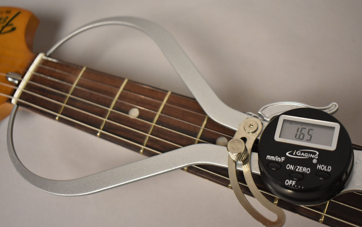 A digital caliper measures the nut width of the dark rosewood fretboard, displaying "1.65" on its screen.