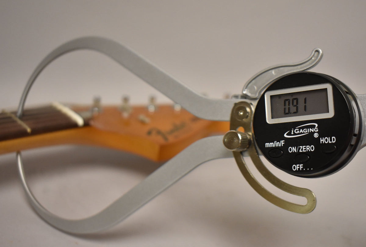 A digital caliper measures the neck thickness at the first fret, displaying "0.91" on its screen.
