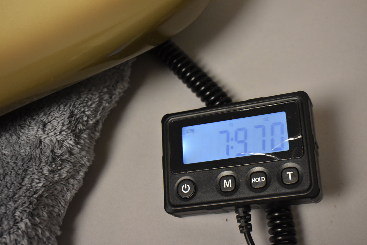 A guitar body rests on a gray towel, with a digital scale displaying "7.9.70" lbs in the foreground.