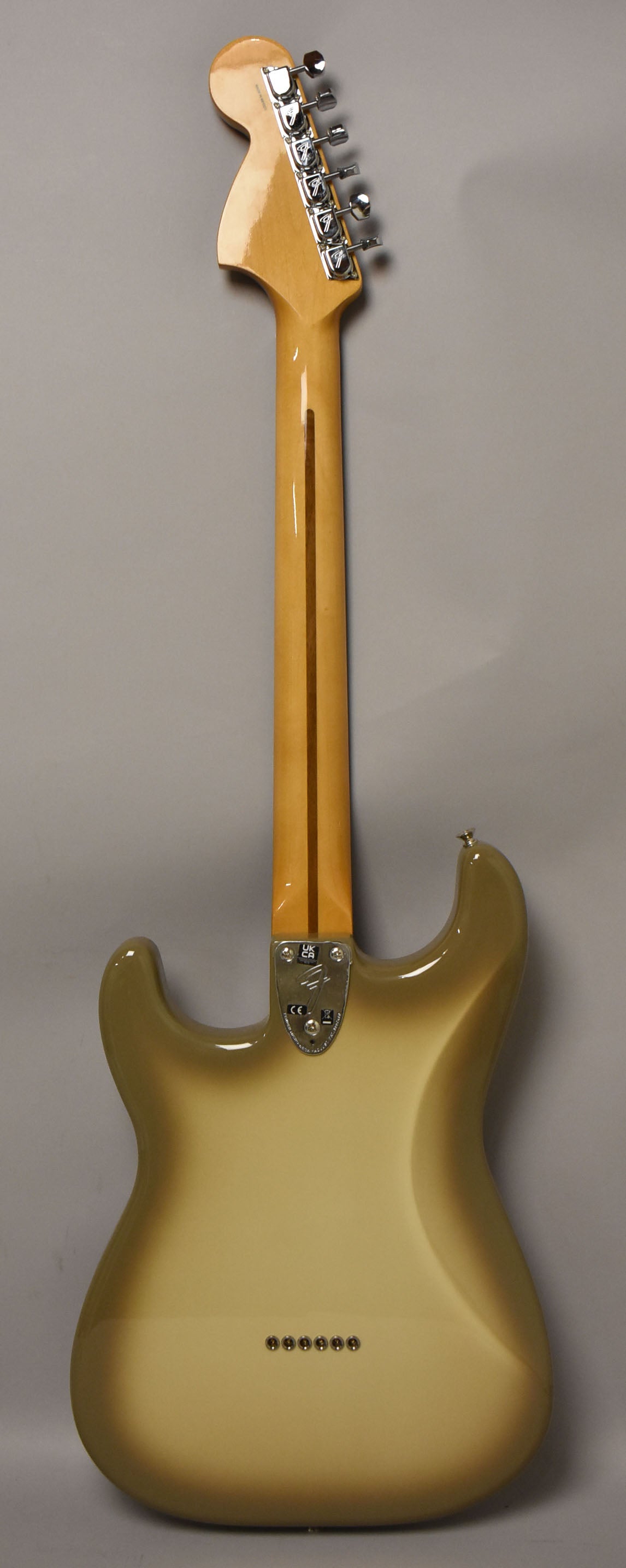 The back of a Stratocaster guitar with a light brown to cream gradient finish, maple neck, and chrome tuners.
