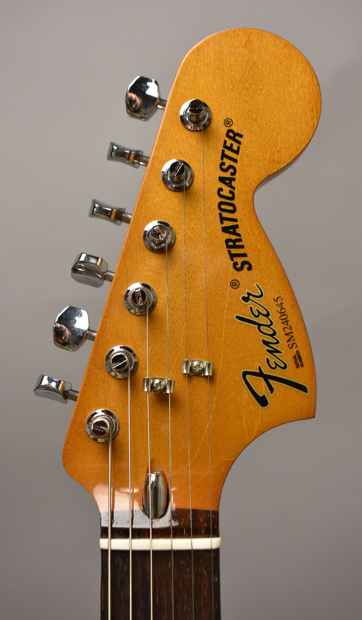 Close-up of the guitar's headstock, angled slightly left, showing six chrome tuners, two string trees, and a dark rosewood fretboard.
