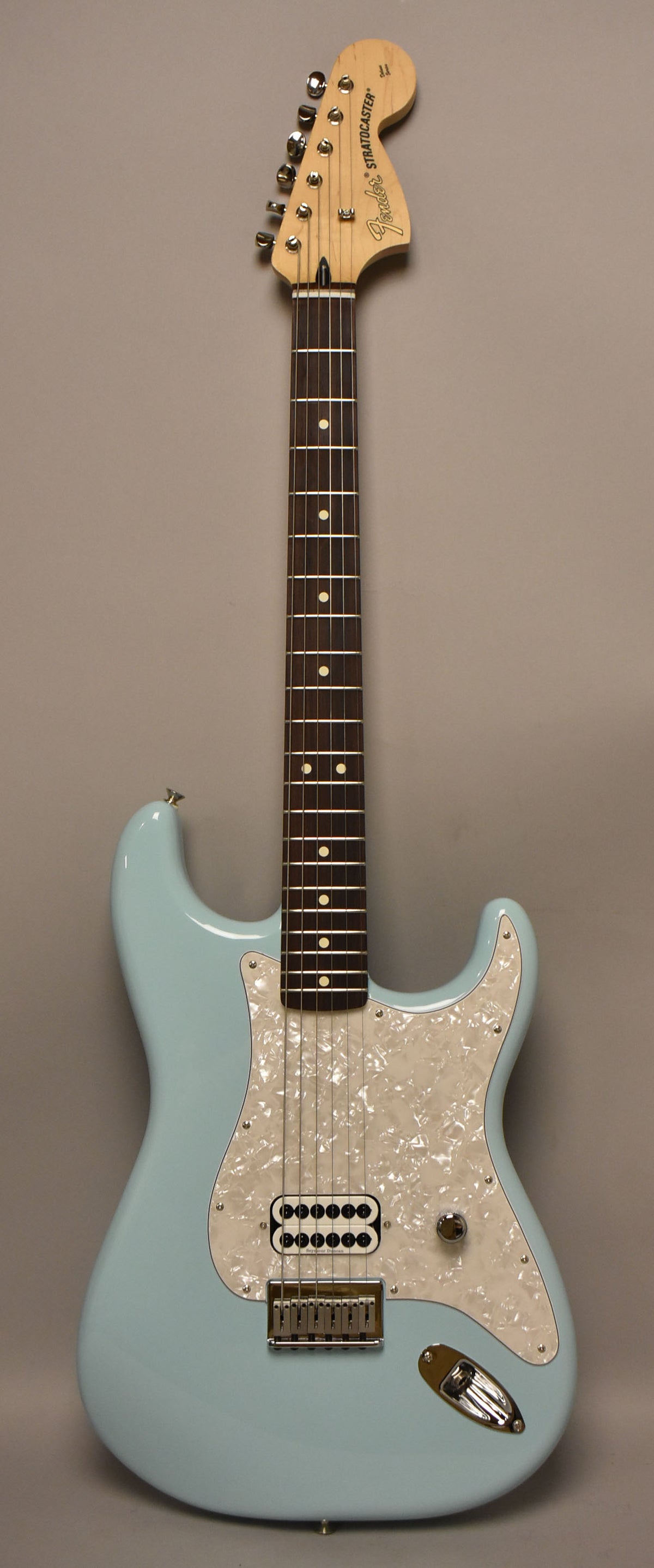 Full-length view of a Daphne Blue Stratocaster with a pearloid pickguard, single humbucker pickup, and one chrome control knob.
