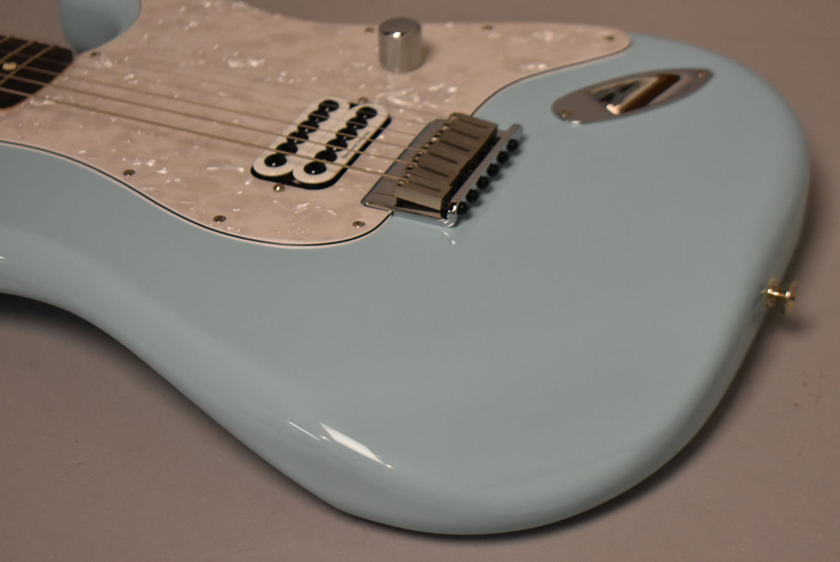 Close-up of a light blue Stratocaster body with a pearloid pickguard, single humbucker pickup, chrome hardtail bridge, and one chrome knob.
