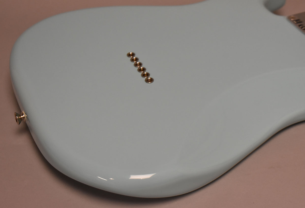 The guitar's Daphne Blue body is shown from the back, with six gold string ferrules and a gold strap button visible.