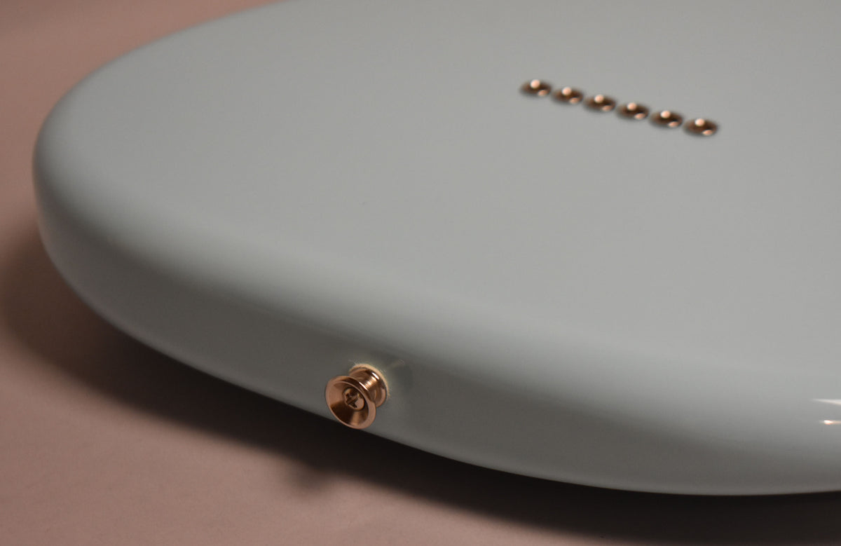Close-up of the Daphne Blue guitar body's lower bout, showing the gold strap button and six gold string ferrules on the back.
