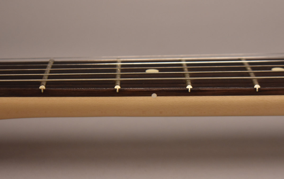 Close-up of the guitar's dark fretboard and light maple neck, showing white dot inlays and frets with strings.