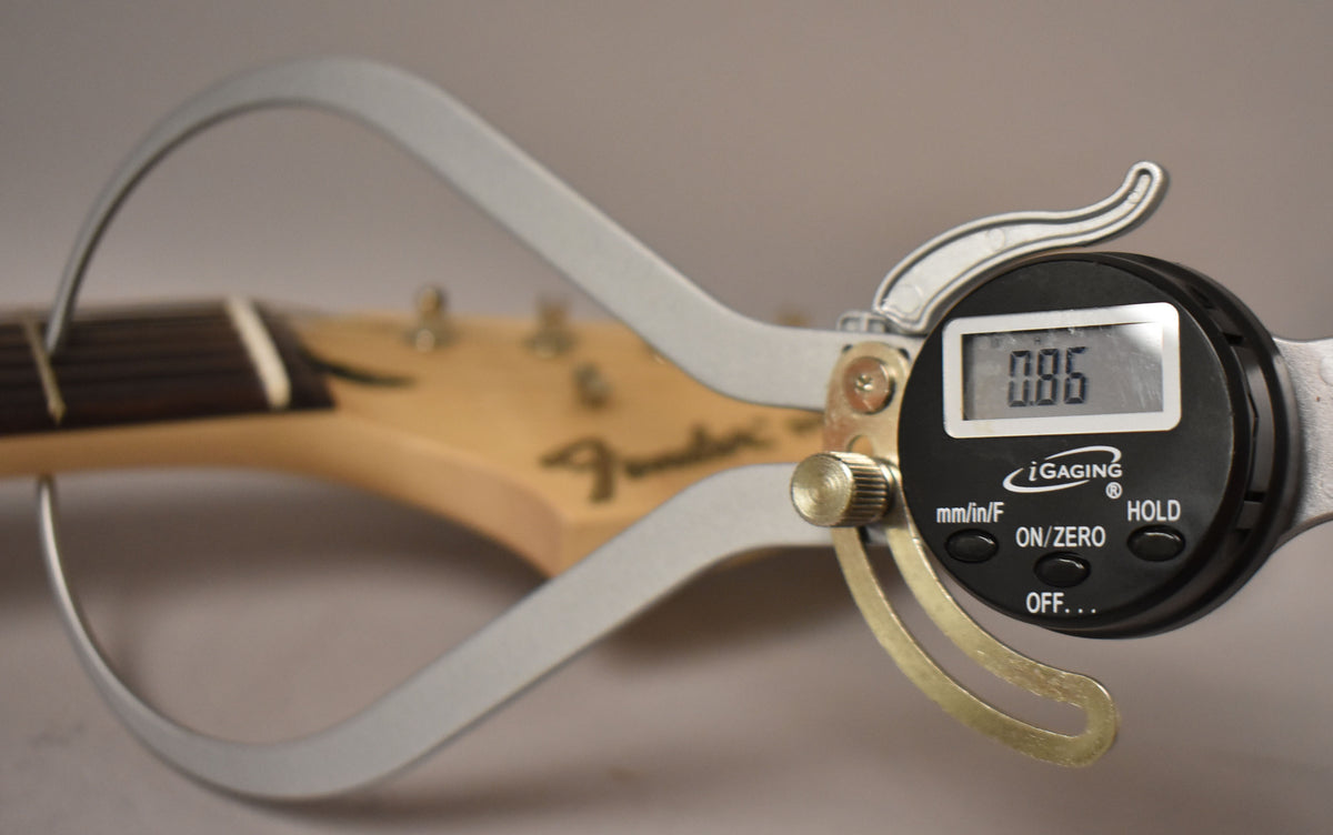 A digital caliper measures the neck thickness of a light wood headstock with a dark fretboard, displaying "0.86".