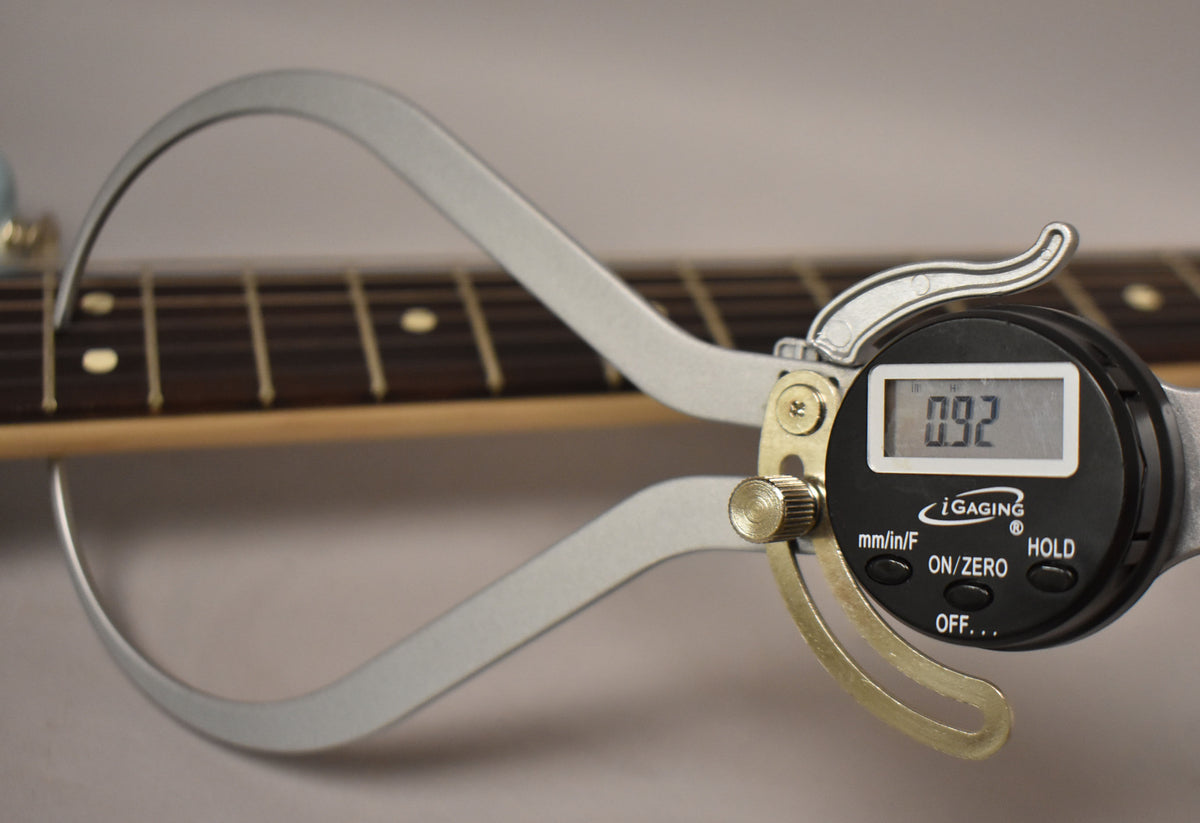 A digital caliper measures the fret height on the dark rosewood fingerboard, showing "0.92" on its display.