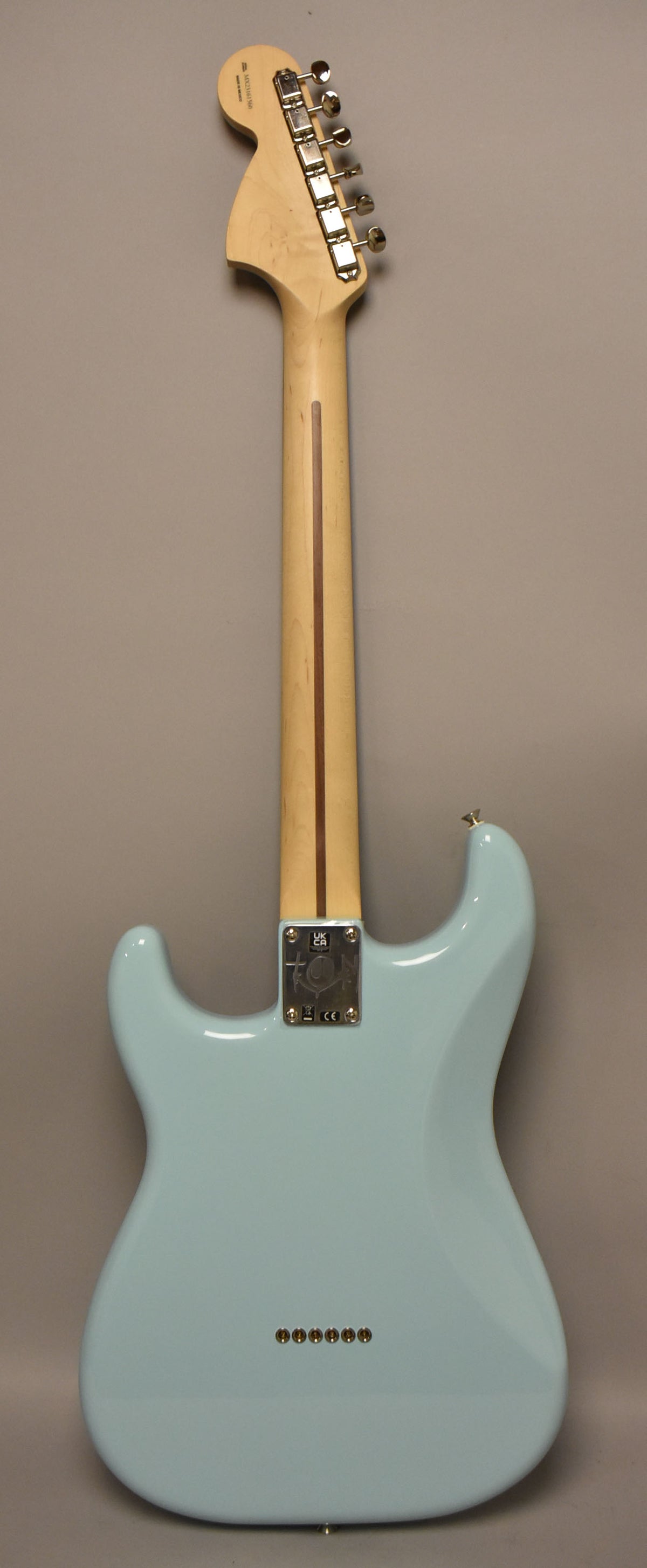 The back of a Daphne Blue Stratocaster with a light maple neck, chrome tuners, and six string-through-body ferrules.