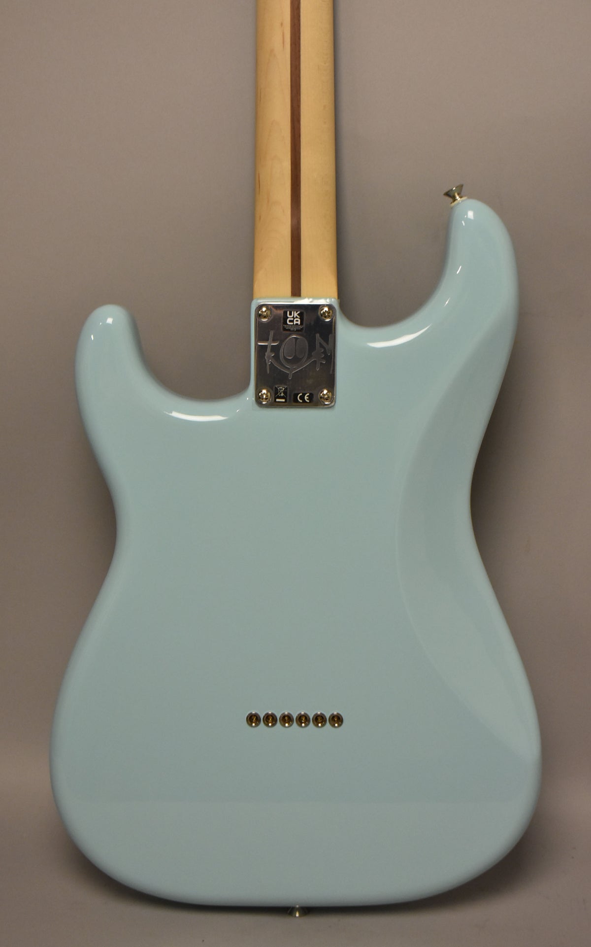 The back of a Daphne Blue Stratocaster, showing the light maple neck, chrome neck plate, and six string-through-body ferrules.