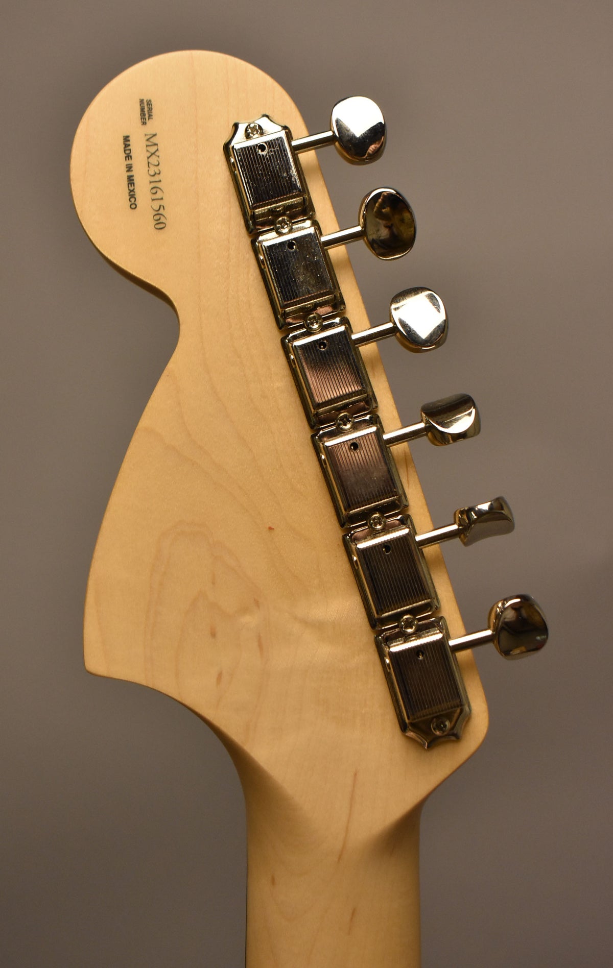 The back of a light wood headstock and neck, angled right, with six chrome tuners and a serial number.