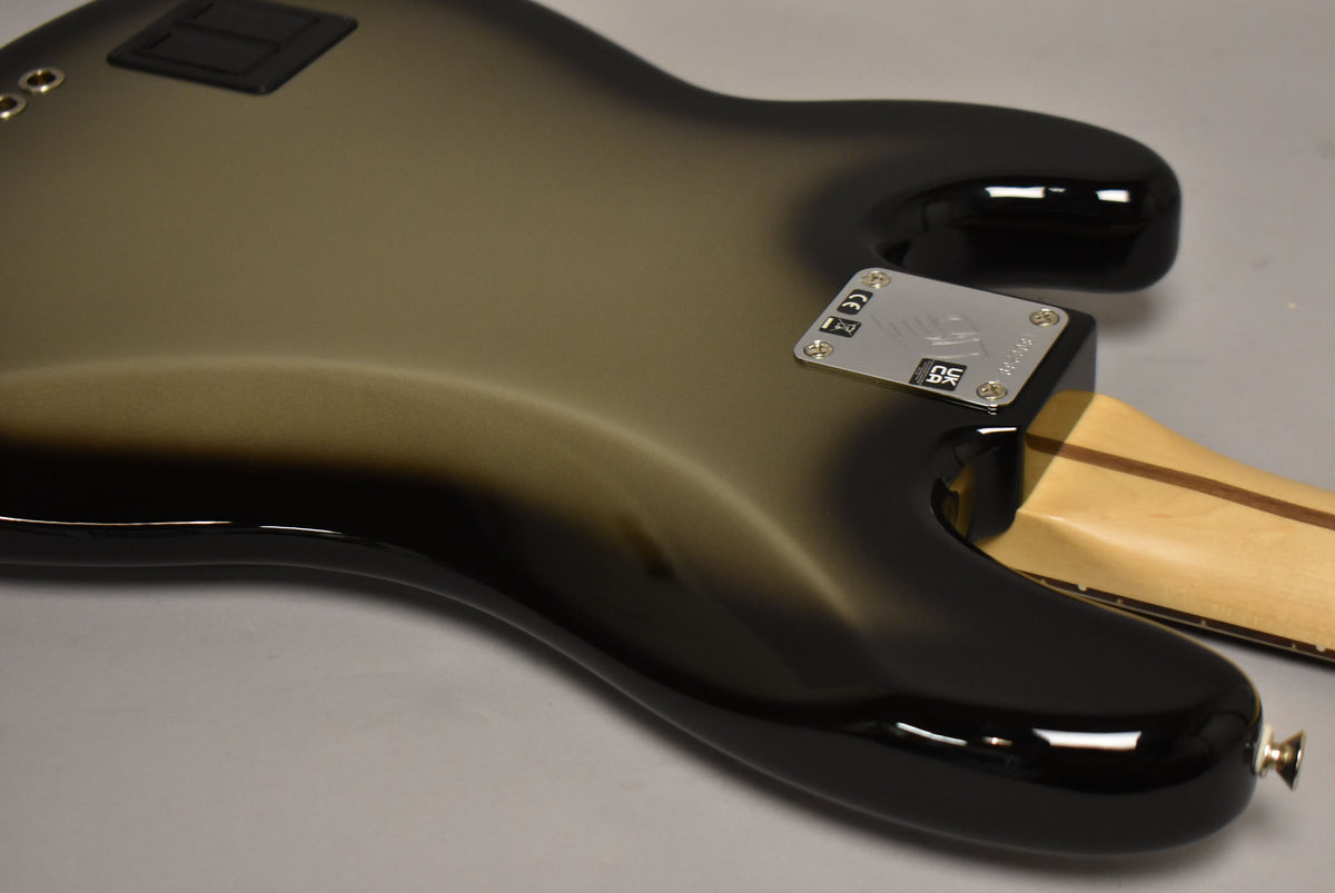 The bass guitar's body, in a glossy silverburst finish, is viewed from the back, showing the neck plate and strap button.