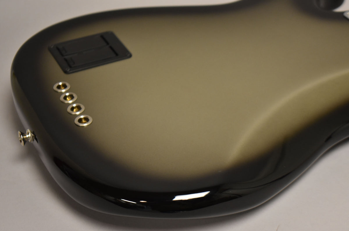 The bass's silverburst back, with a black battery compartment and four gold string ferrules, is angled from the lower left.