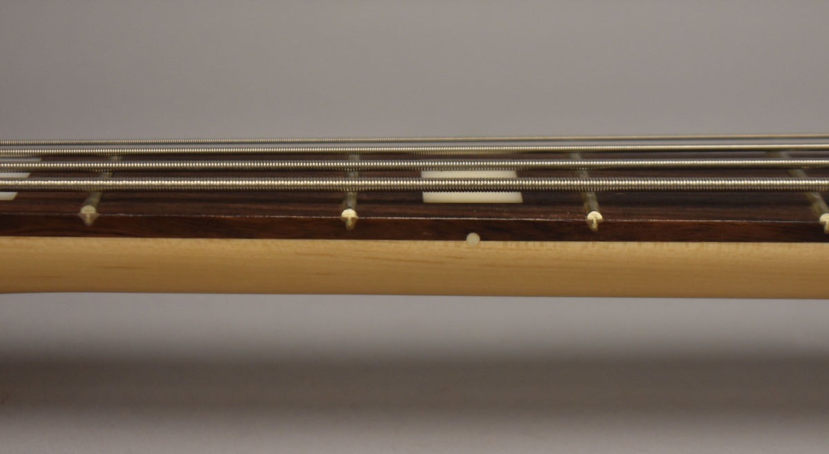 Close-up of the bass's dark fretboard and light maple neck, showing four strings, white rectangular fret markers, and side dots.