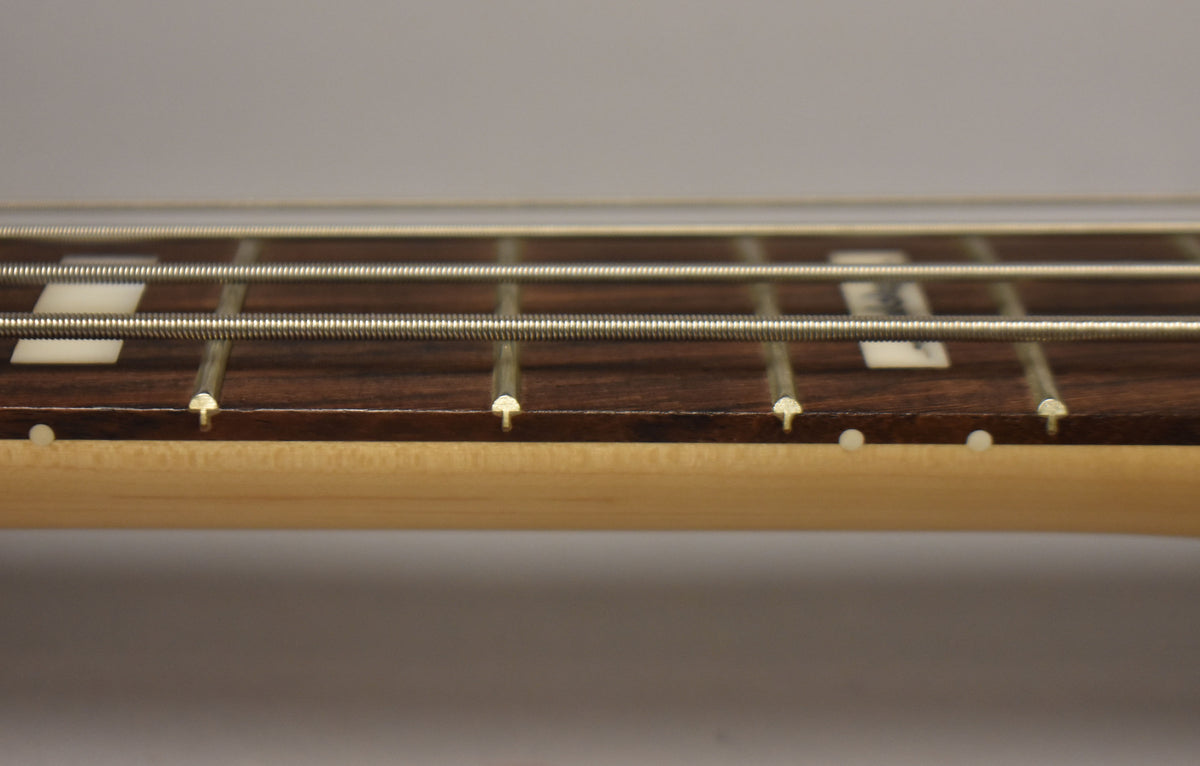 Close-up of the bass's dark fretboard with four strings, showing rectangular white inlays and small white side dots.