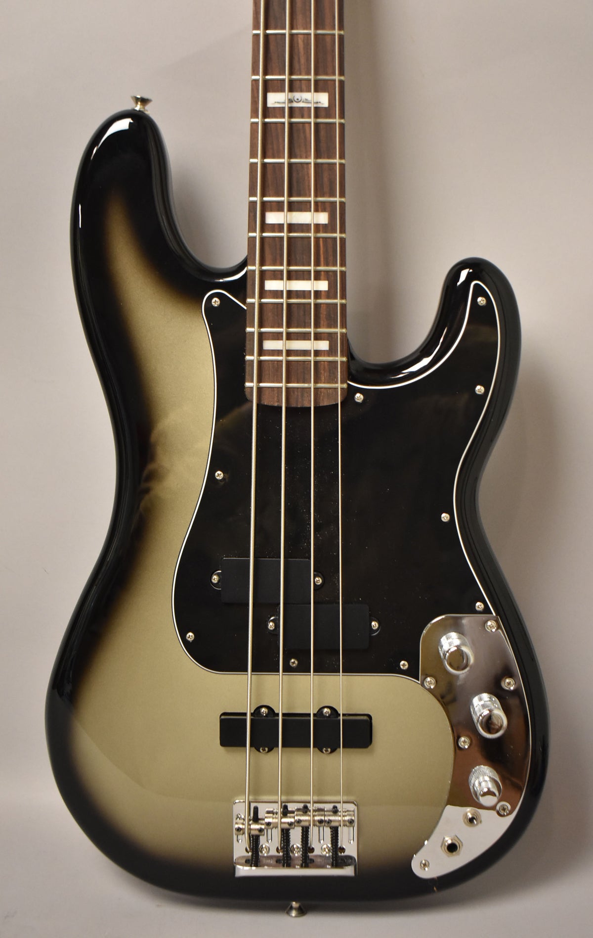 The bass guitar's glossy silverburst body, black pickguard, and chrome hardware are framed from the upper bout to the lower strap button.