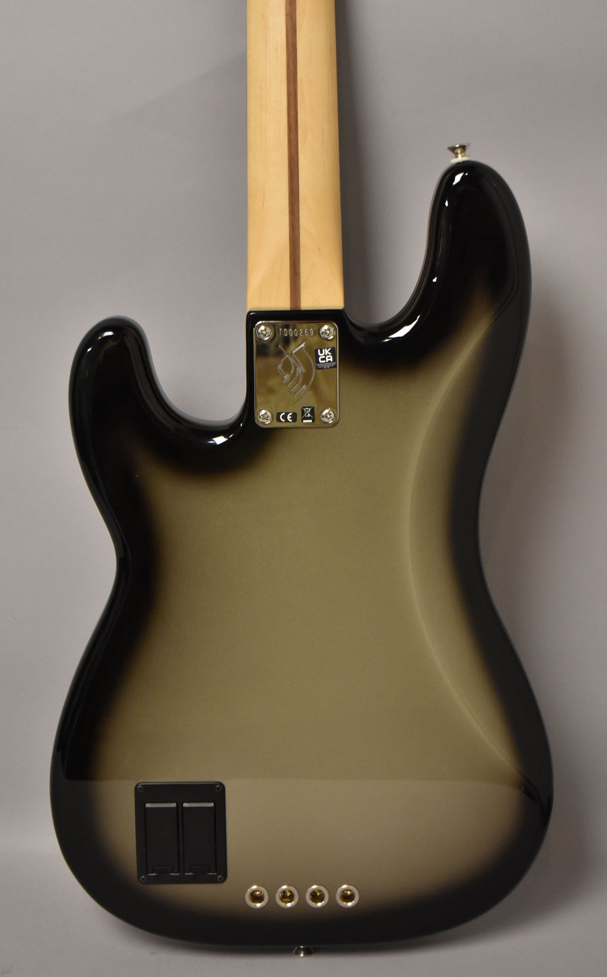 The bass guitar's silverburst back shows a maple neck, a chrome neck plate, a black battery compartment, and four chrome control knobs.