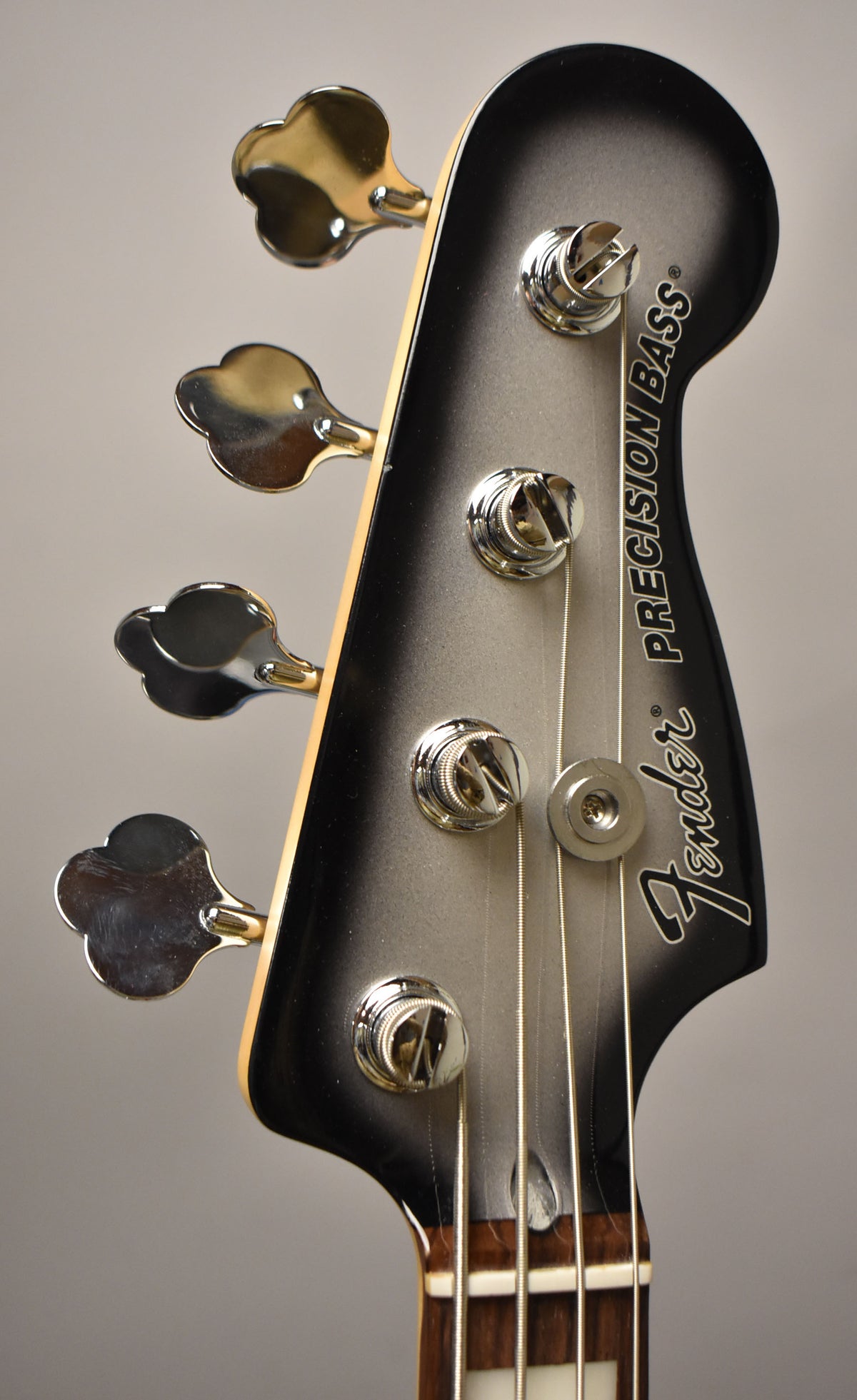The bass headstock, in silverburst finish with chrome clover-leaf tuners, is angled slightly, showing the nut and part of the fretboard.