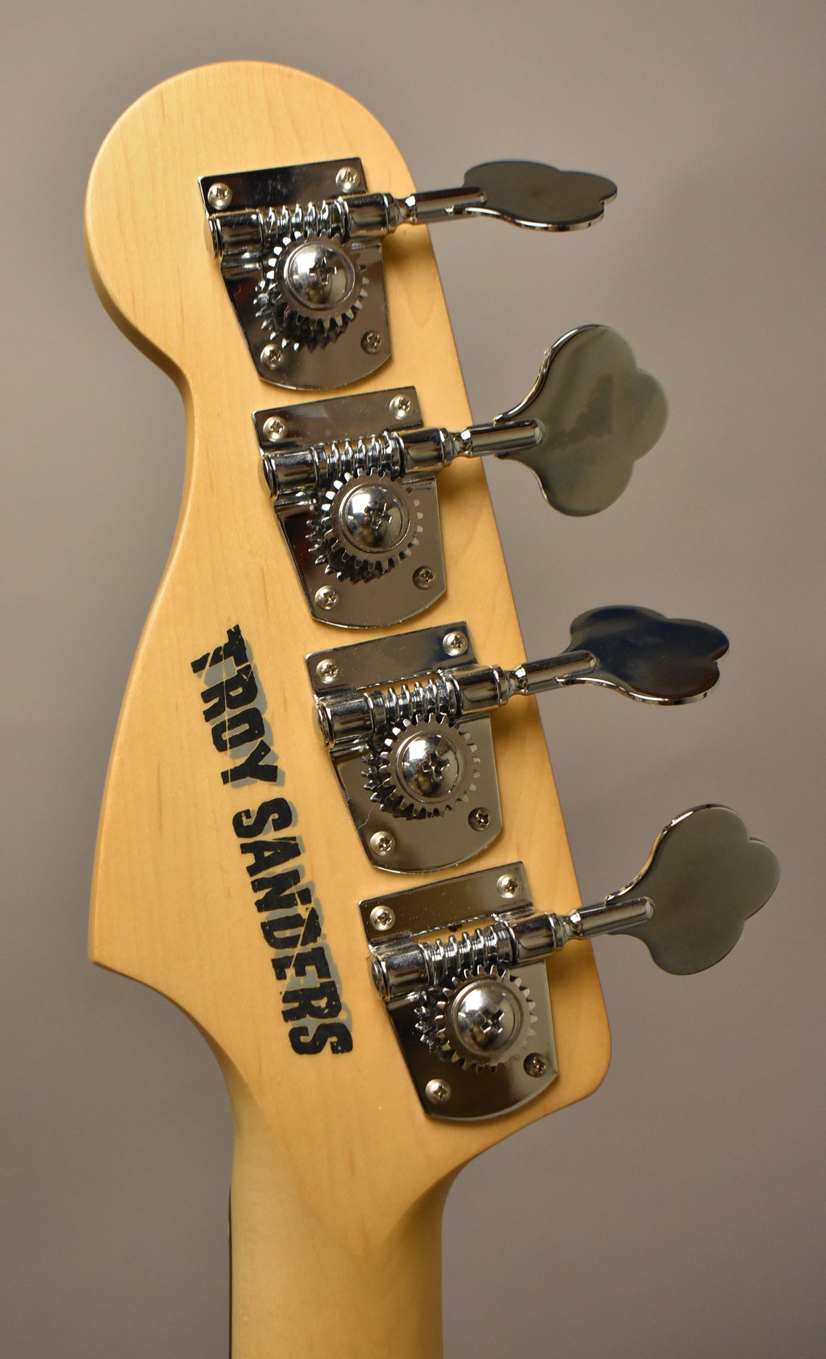 The bass headstock, angled from the back, shows a light wood finish with four chrome clover-leaf tuners.