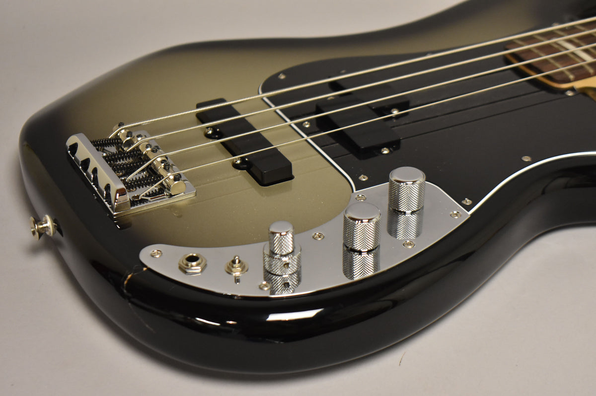The bass body, in silverburst with a black pickguard, shows chrome hardware and four knurled control knobs.