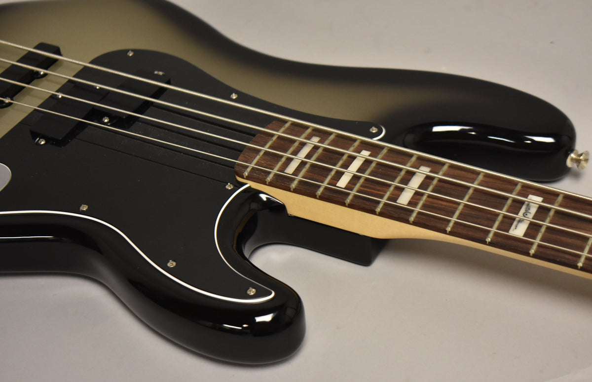 The bass guitar's upper body and neck are angled, showing the silverburst finish, black pickguard, and block inlays on the fretboard.