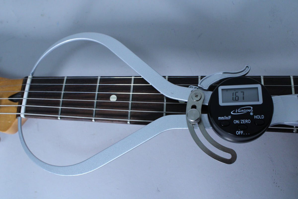 A digital caliper measures the dark fretboard with light frets and dot inlays, displaying "1.67" on its screen.