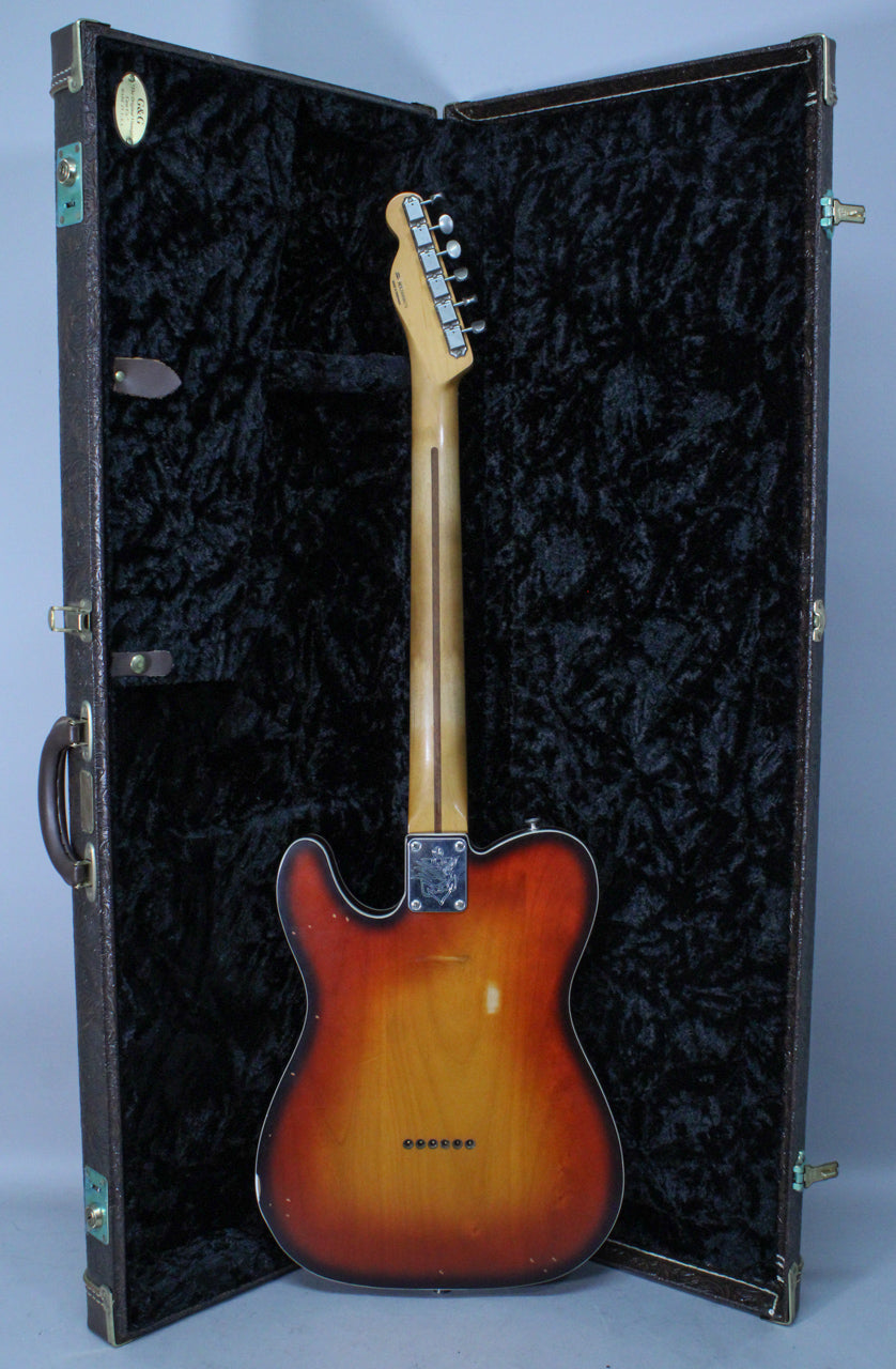 The guitar's back, in a 3-color chocolate burst finish, stands in an open, dark brown hardshell case with black crushed velvet lining.