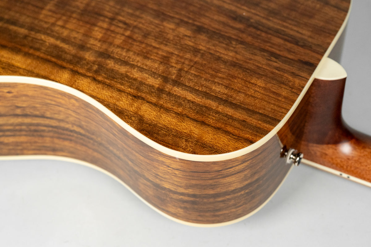 Close-up of the guitar's lower bout, showing the dark brown wood grain of the back and sides with cream binding and a strap button.